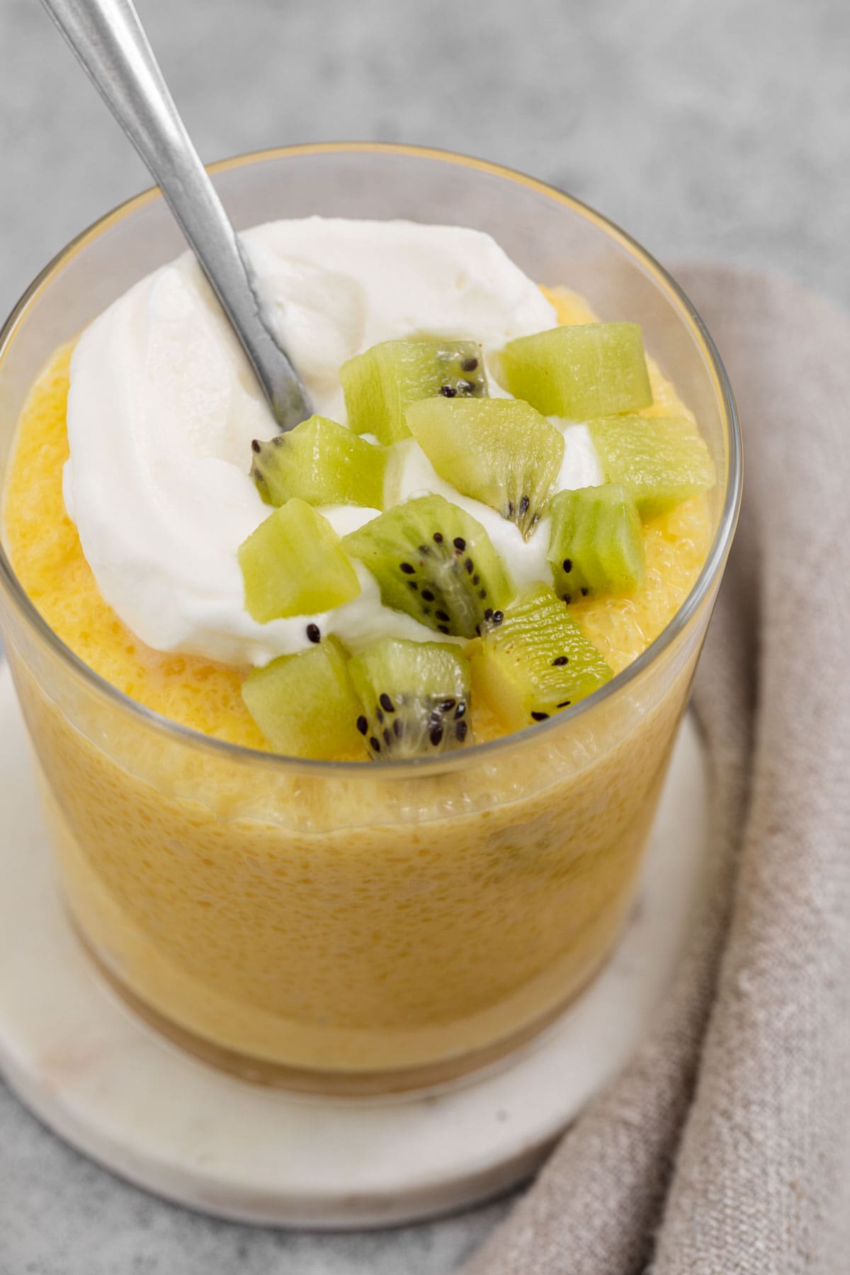 Ariel view of tapioca in a glass topped with whipped cream and kiwi chunks.