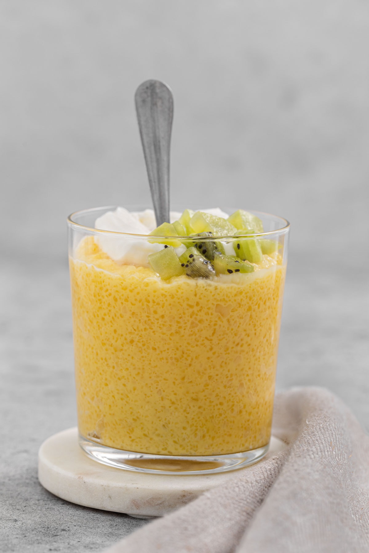 Tapioca pudding in a clear glass topped with whipped cream and kiwi chunks.