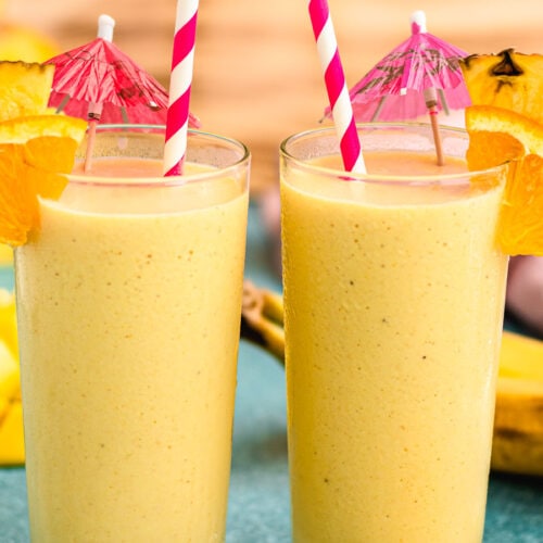 Two tropical smoothies with straws and umbrella garnishes.