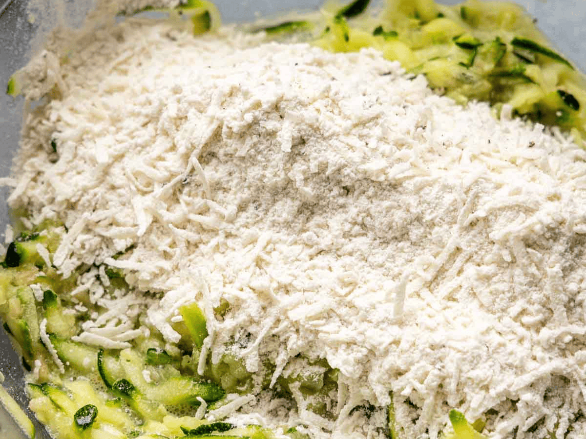 Shredded zucchini, shredded cheese, and flour in bowl.