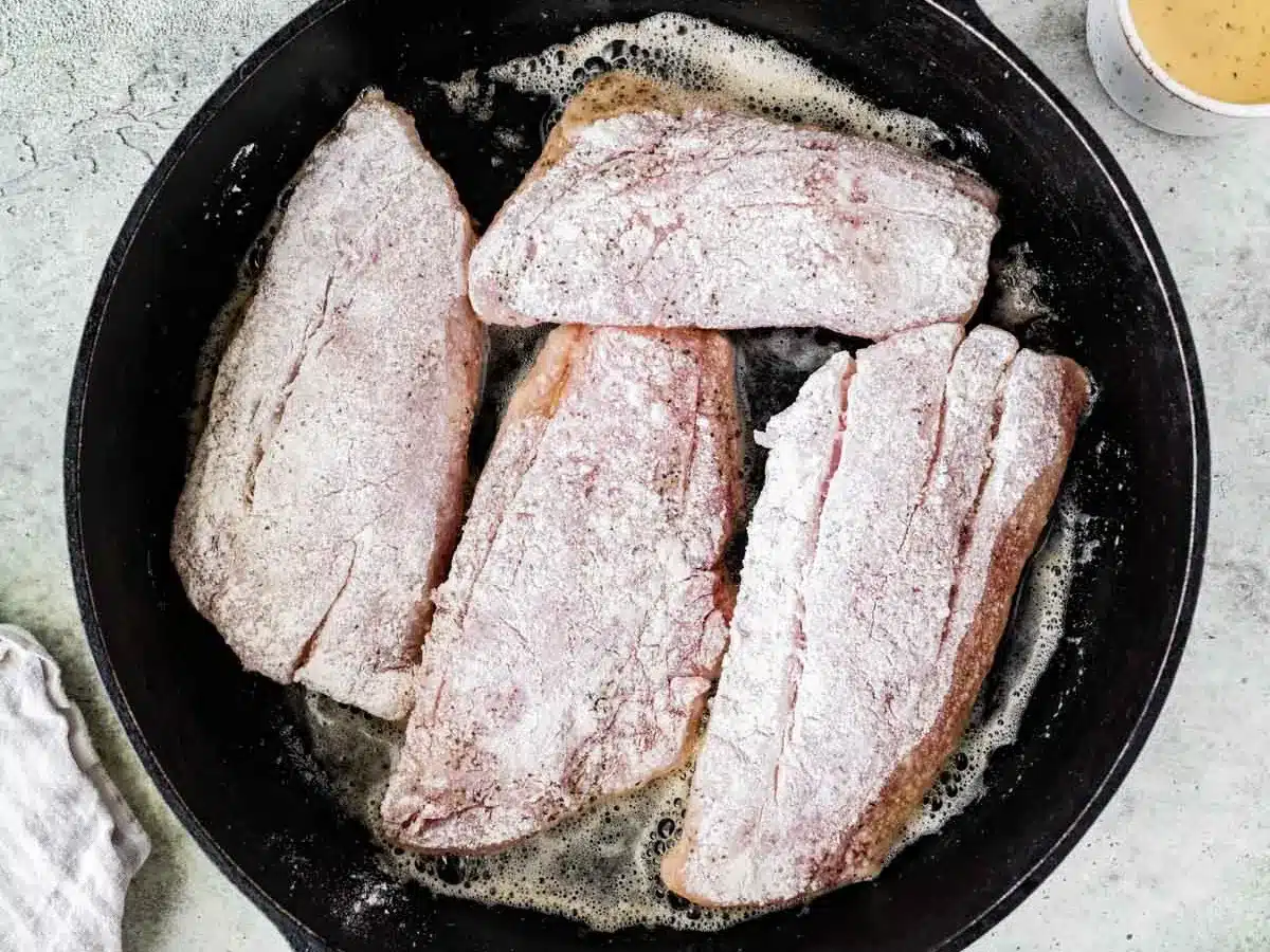 Raw fish coated in flour and seasonings, frying in pan.