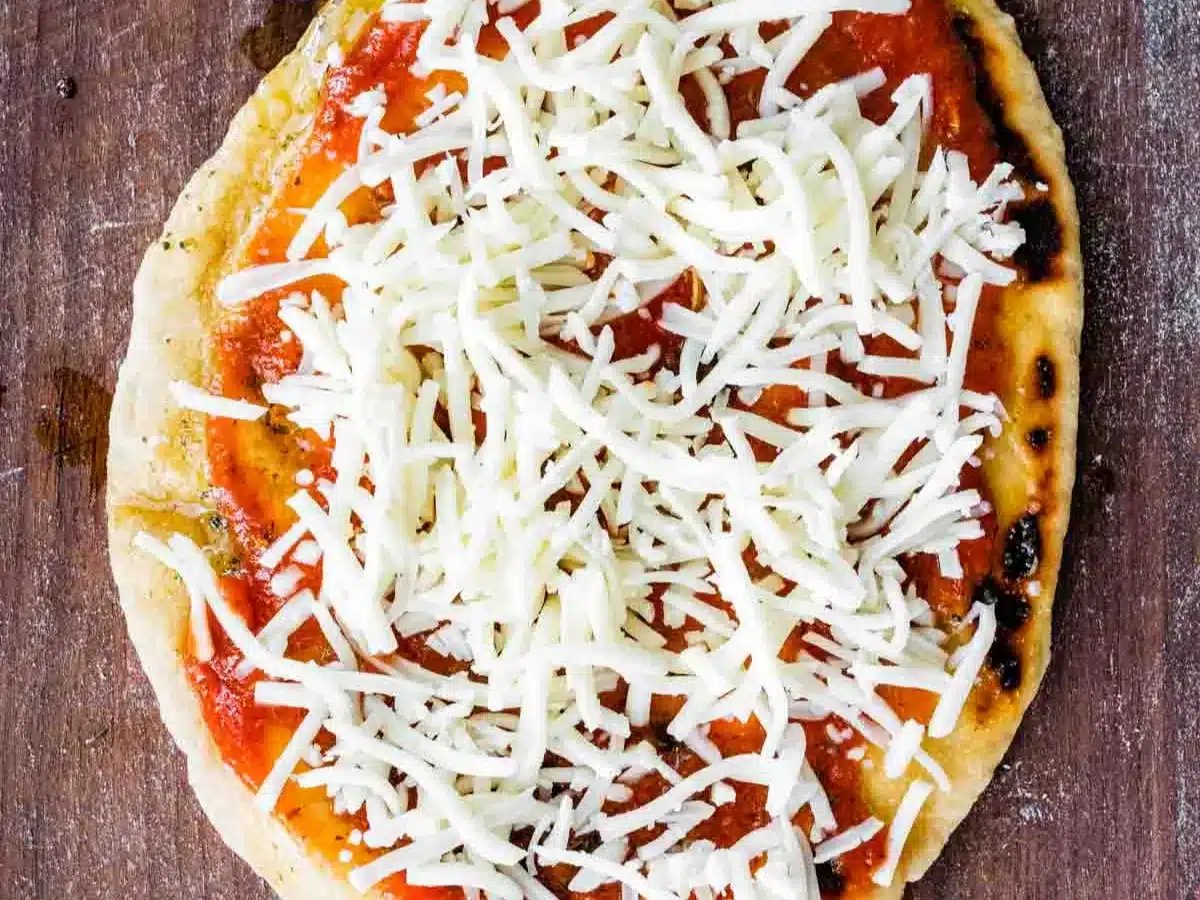 Sauce and shredded cheese on thin bread round.