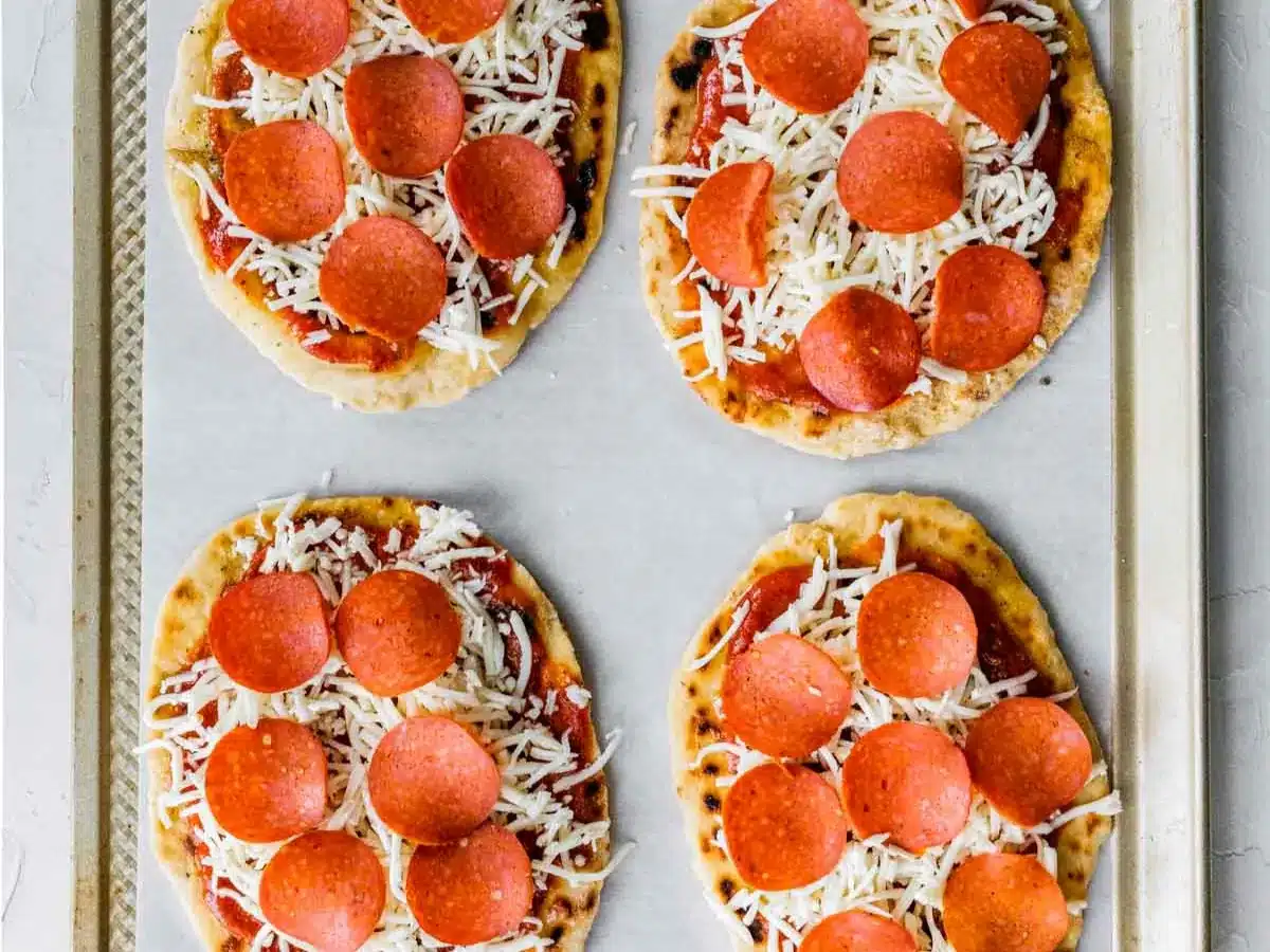 Four small pizzas on baking sheet.