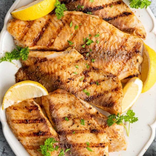 Grilled fish fillets on serving plate with lemon wedges.