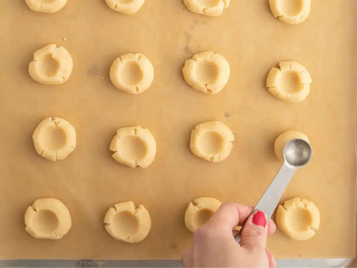 Teaspoon pressing an indent into cookie dough.