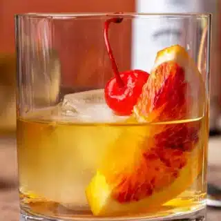 Rocks glass filled with bourbon, orange and cherry garnish.