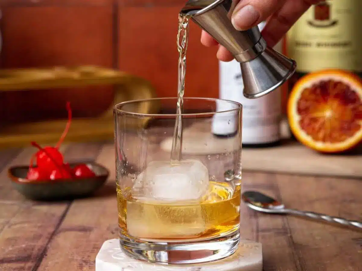 Bourbon being added to glass with large cube of ice.