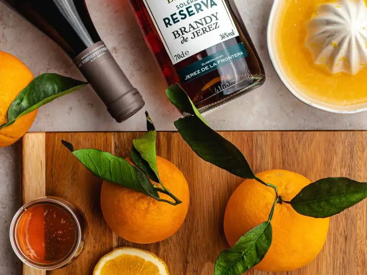 Cutting board with oranges, brandy, and wine bottle on counter.