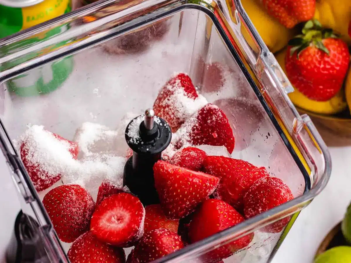 Blender filled with sliced strawberries and sugar.