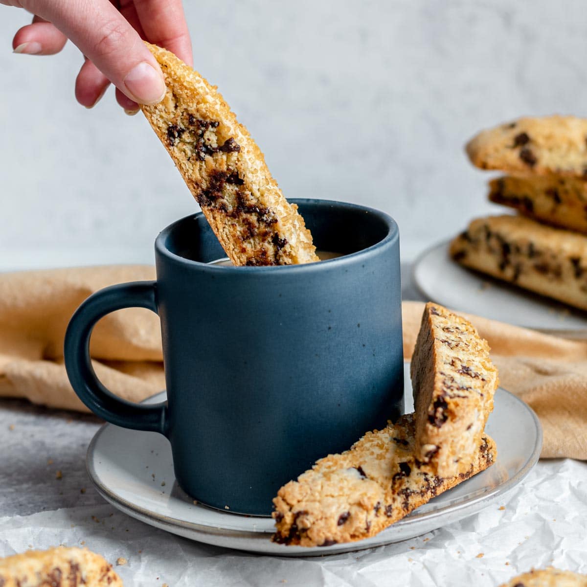 Chocolate Chip Biscotti baked cookie being dunked into cup of coffee with other cookies on plate