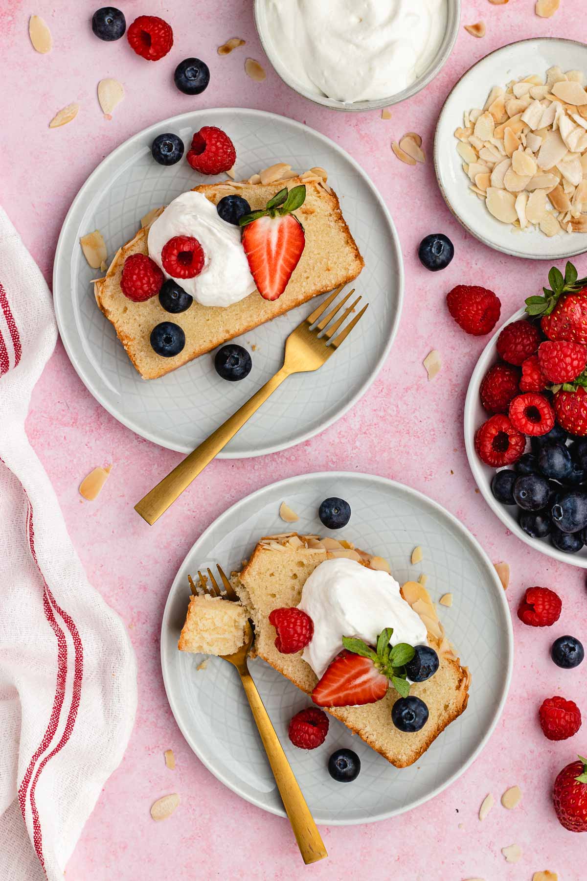 Almond Pound Cake slices on two plates with whipped cream and berries on top and forks.