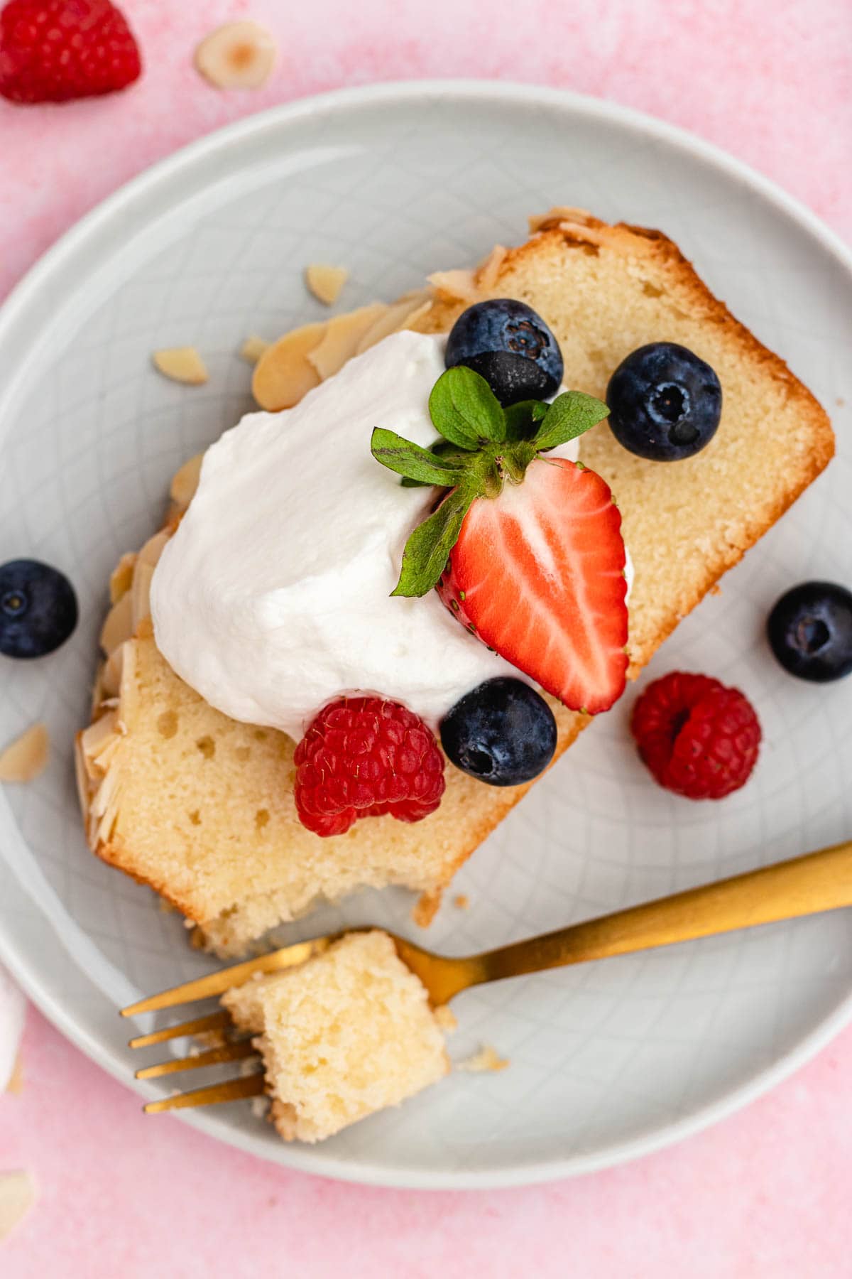 Almond Pound Cake slice on plate with whipped cream and berries on top and fork with bite.