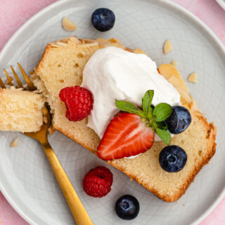 Cake slice on plate with whipped cream and berries on top and fork with bite.