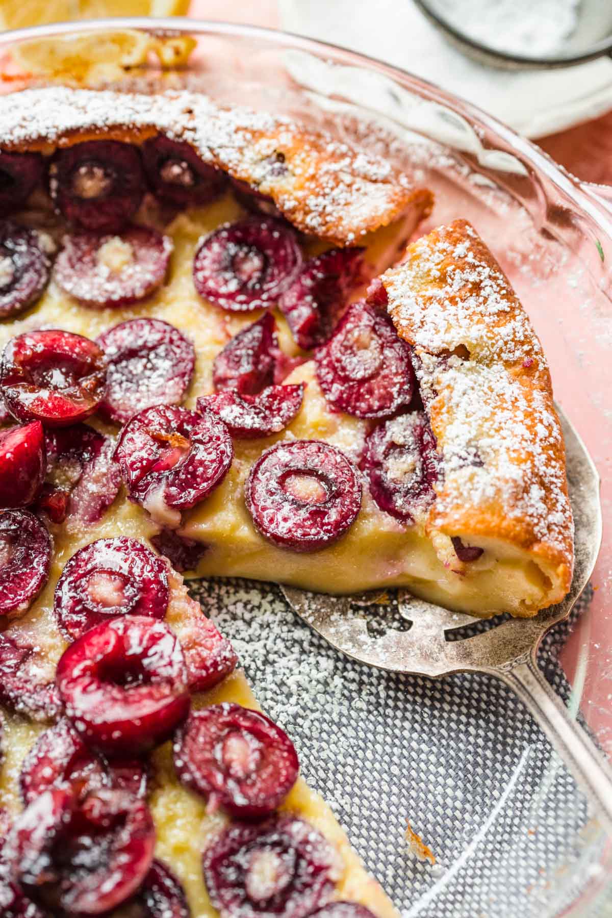 Cherry Clafoutis baked in dish with slice removed and serving spatula under another slice