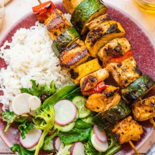 Meat and veggie kabobs on plate with rice and salad.