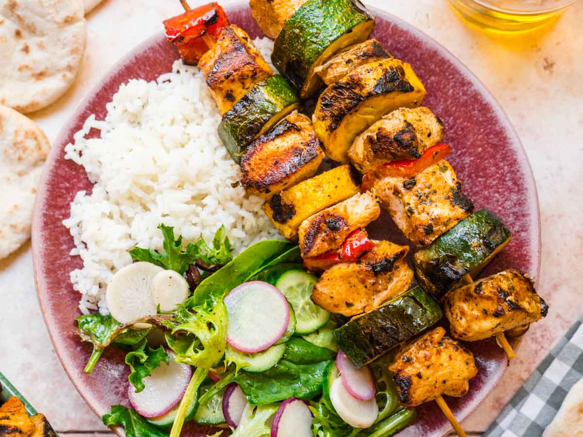 Meat and veggie kabobs on plate with rice and salad.
