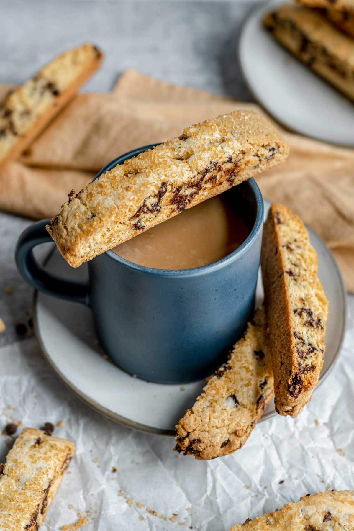 Chocolate Chip Biscotti baked cookie being resting on cup of coffee with other cookies on plate