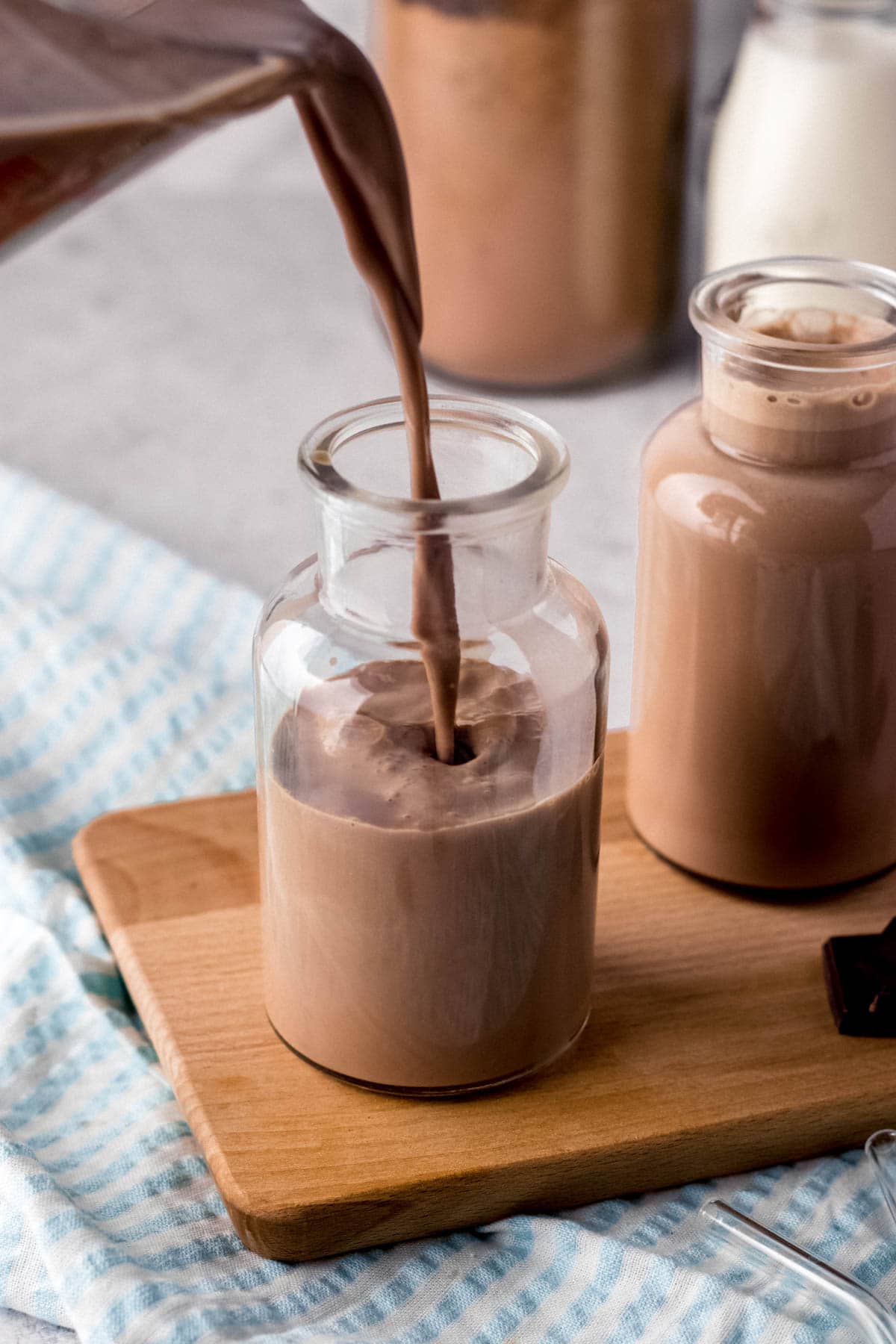 Chocolate Milk two small glass milk jars pouring chocolate milk into front jar on cutting board