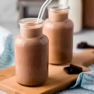 two glasses of sweet brown liquid with a glass straw on a cutting board