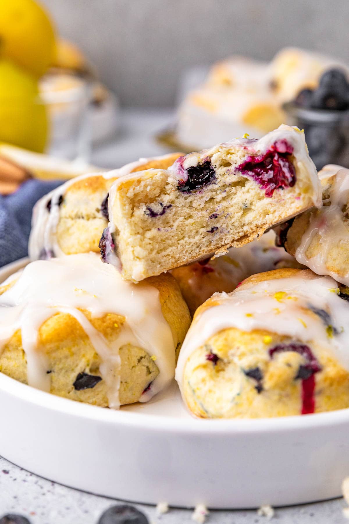 Lemon Blueberry Biscuits baked and glazed biscuits stacked on plate with top biscuit missing bite