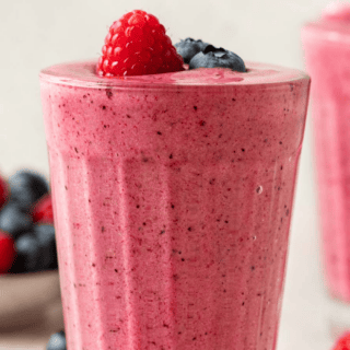 Pink blended drink in a glass cup topped with a raspberry and blueberries.