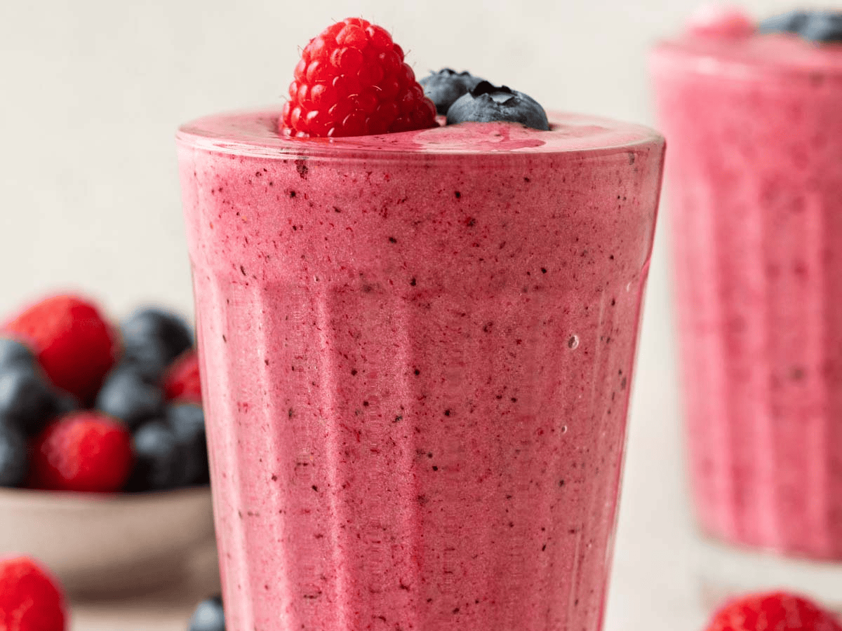 Pink blended drink in a glass cup topped with a raspberry and blueberries.