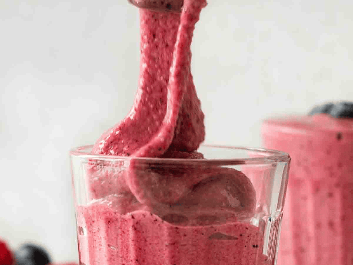 Pink colored blended fruit drink being poured into a glass cup.
