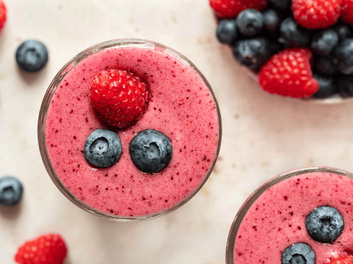 Top view of pink blended fruit drink garnished with blueberries and a raspberrry.