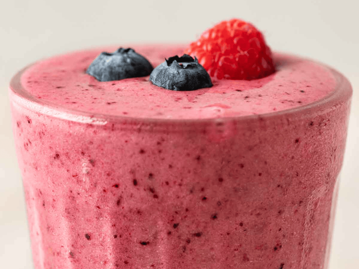 Close up of pink blended fruit drink garnished with blueberries and a raspberry.