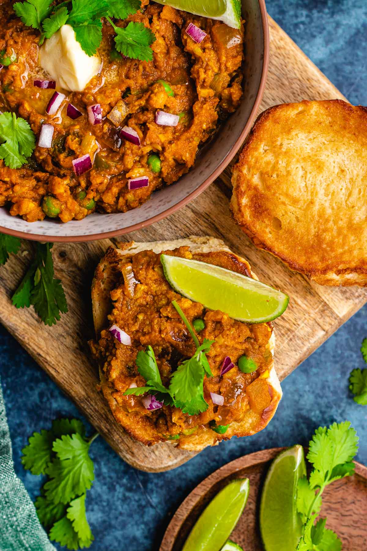 Pav Bhaji cooked and garnished in bowl with toasted bread on side, some pav bhaji on one piece of bread