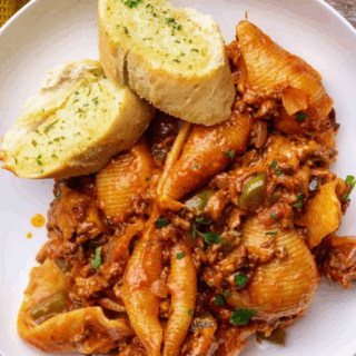 shelled noodles, cooked ground beef, with garnish on top of a plate with garlic bread