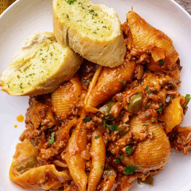 shelled noodles, cooked ground beef, with garnish on top of a plate with garlic bread