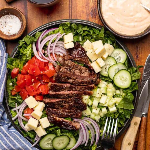 Steak Salad finished salad on plate with dressing in bowl in upper right corner and beer in upper left corner