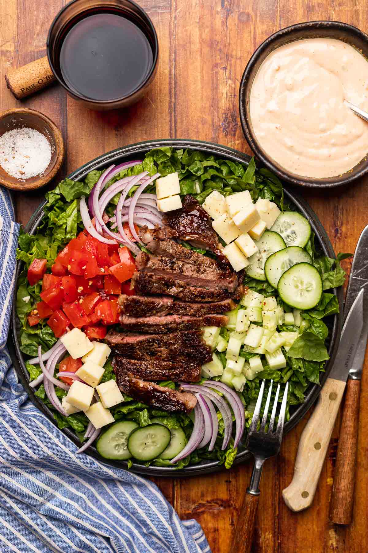 Steak Salad finished salad on plate with dressing in bowl in upper right corner and beer in upper left corner