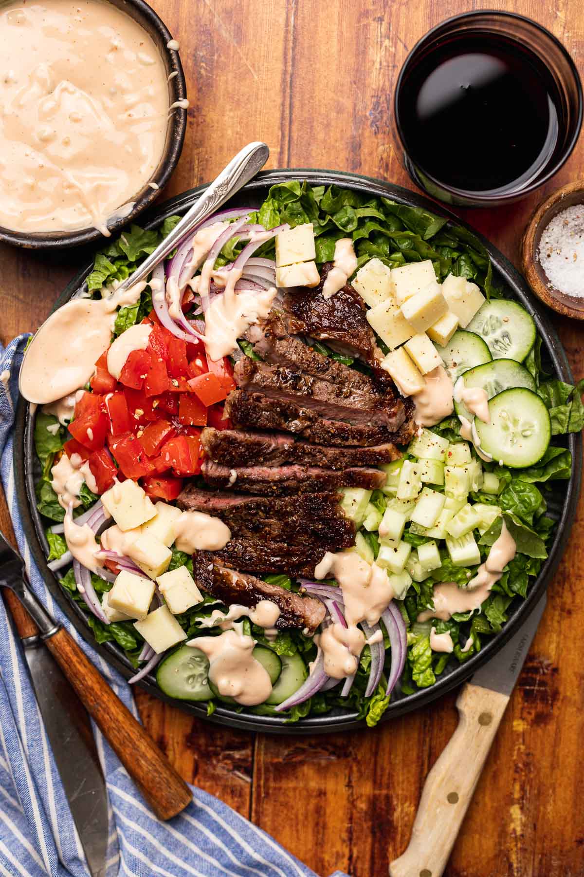 Steak Salad finished salad on plate with dressing in bowl in upper left corner and beer in upper right corner