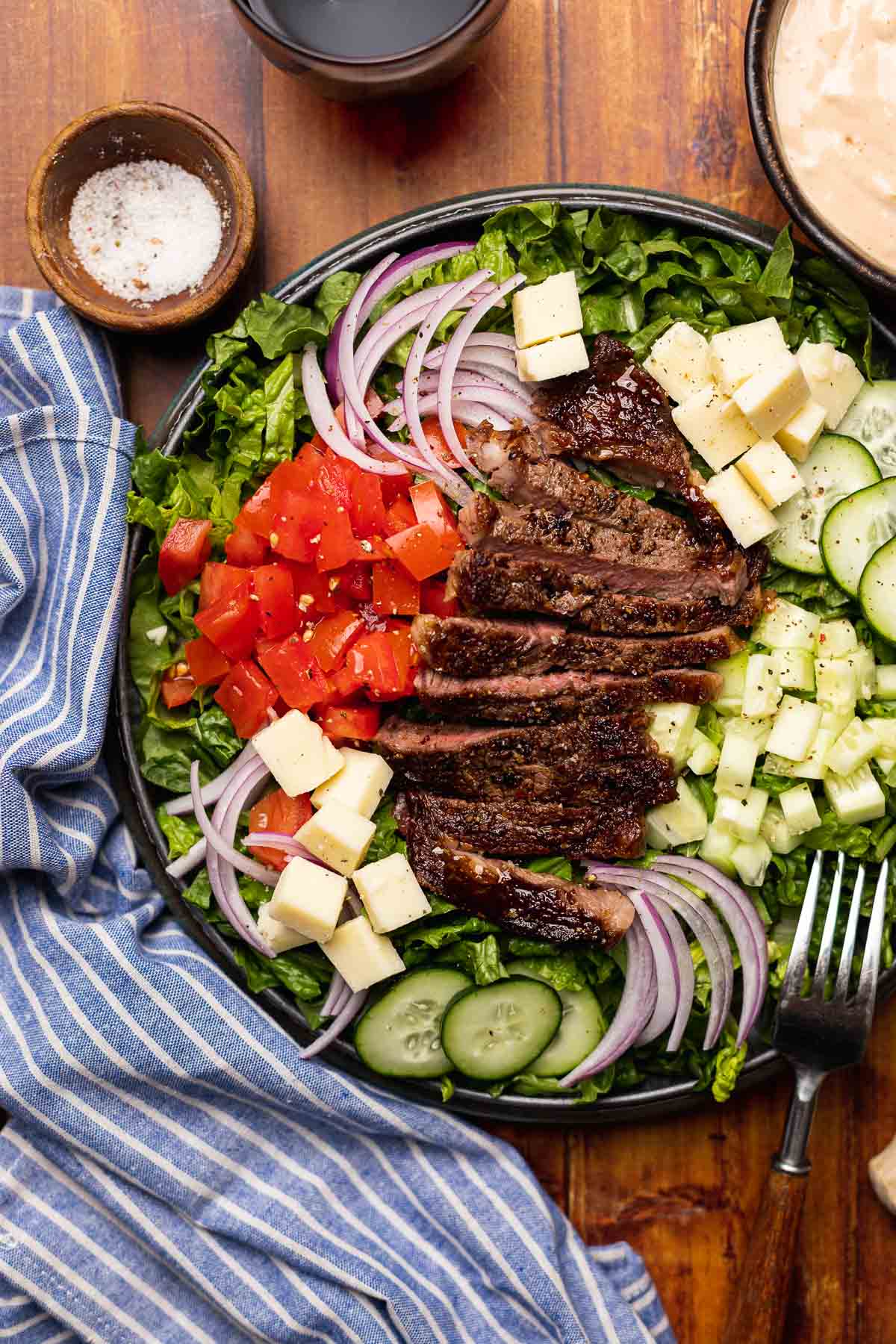 Steak Salad finished salad on plate with dressing in bowl in upper right corner and beer in upper left corner