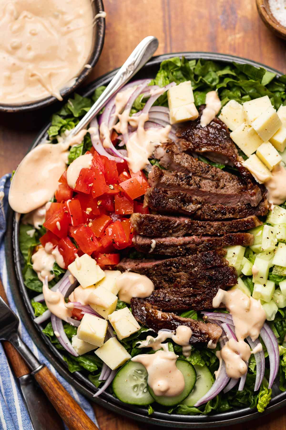 Steak Salad finished salad on plate with dressing in bowl in upper left corner