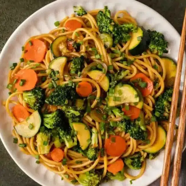 Noodles and stir fry served on plate with chop sticks