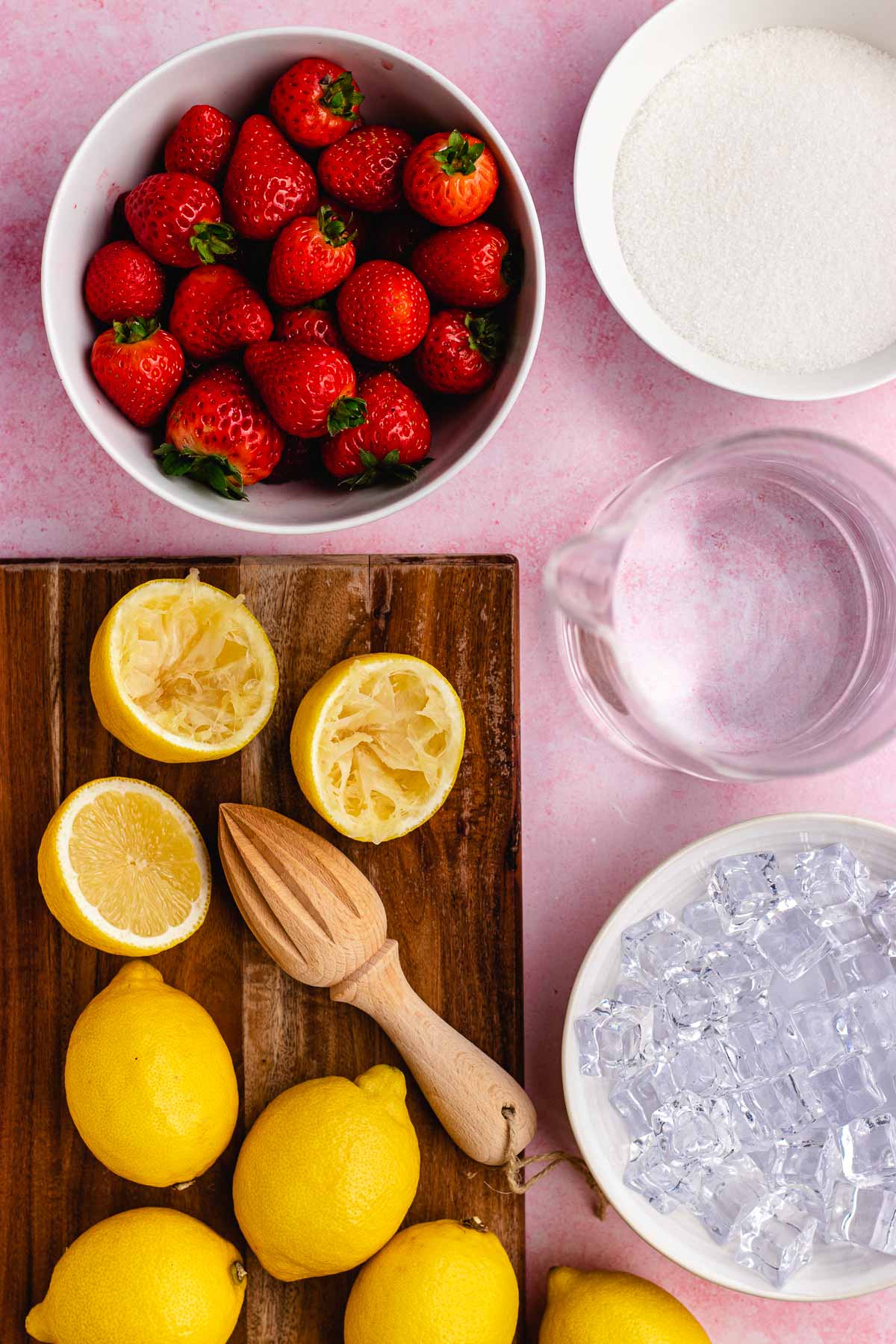 Strawberry Lemonade ingredients separated in prep bowls, halved lemons on wooden board with hand juicer