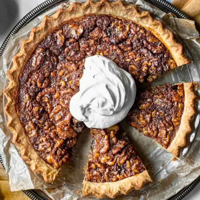 circular crusted dessert with nuts with a dollop of whipped cream and slices