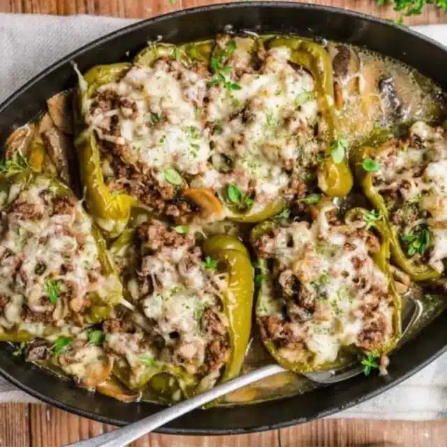 Stuffed peppers in a roasting pan with melted cheese garnish