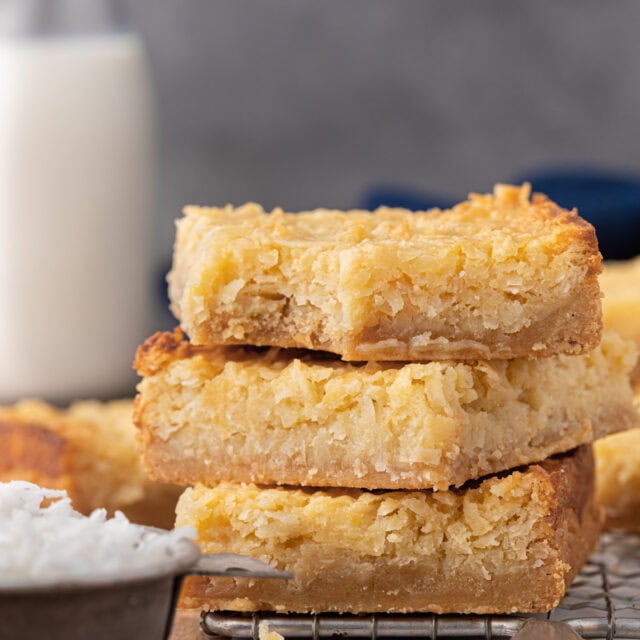 Coconut Macaroon Bars stack of three bars on cooling rack, side view and bite taken out of top bar, 1x1