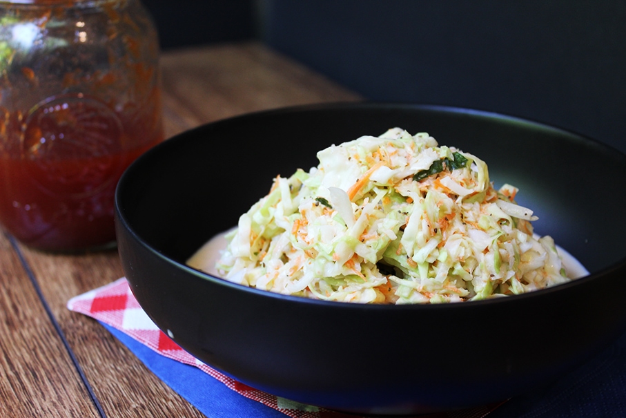 black bowl filled with coleslaw. A clear jar with dark red bbq sauce. 
