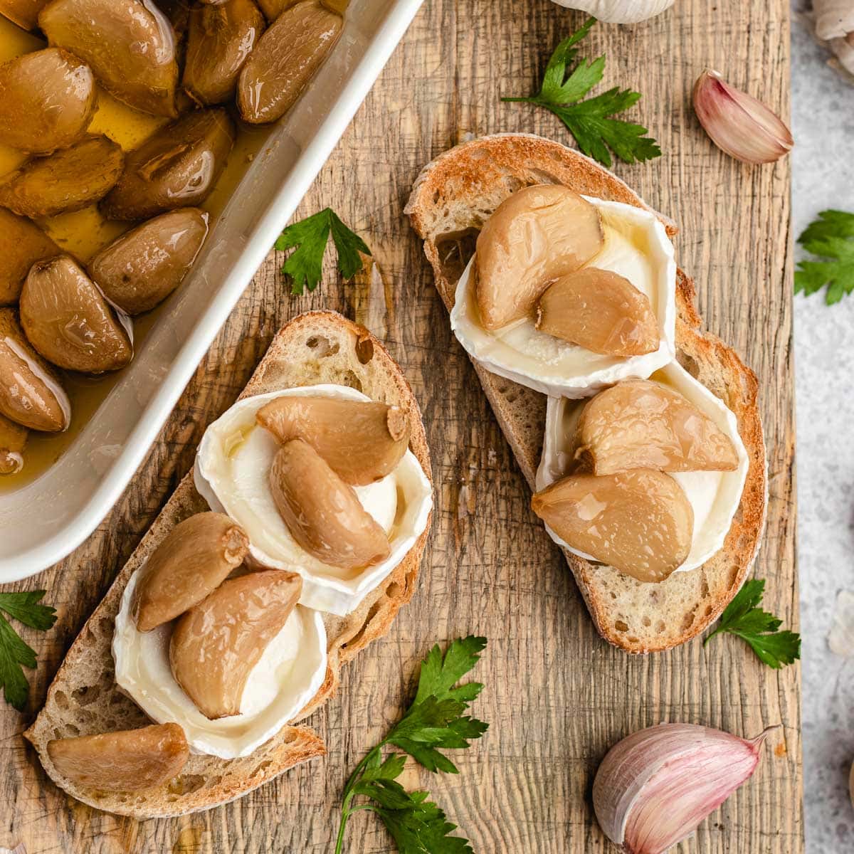 Garlic Confit roasted cloves on toast slices with goat cheese, cloves in oil in baking dish