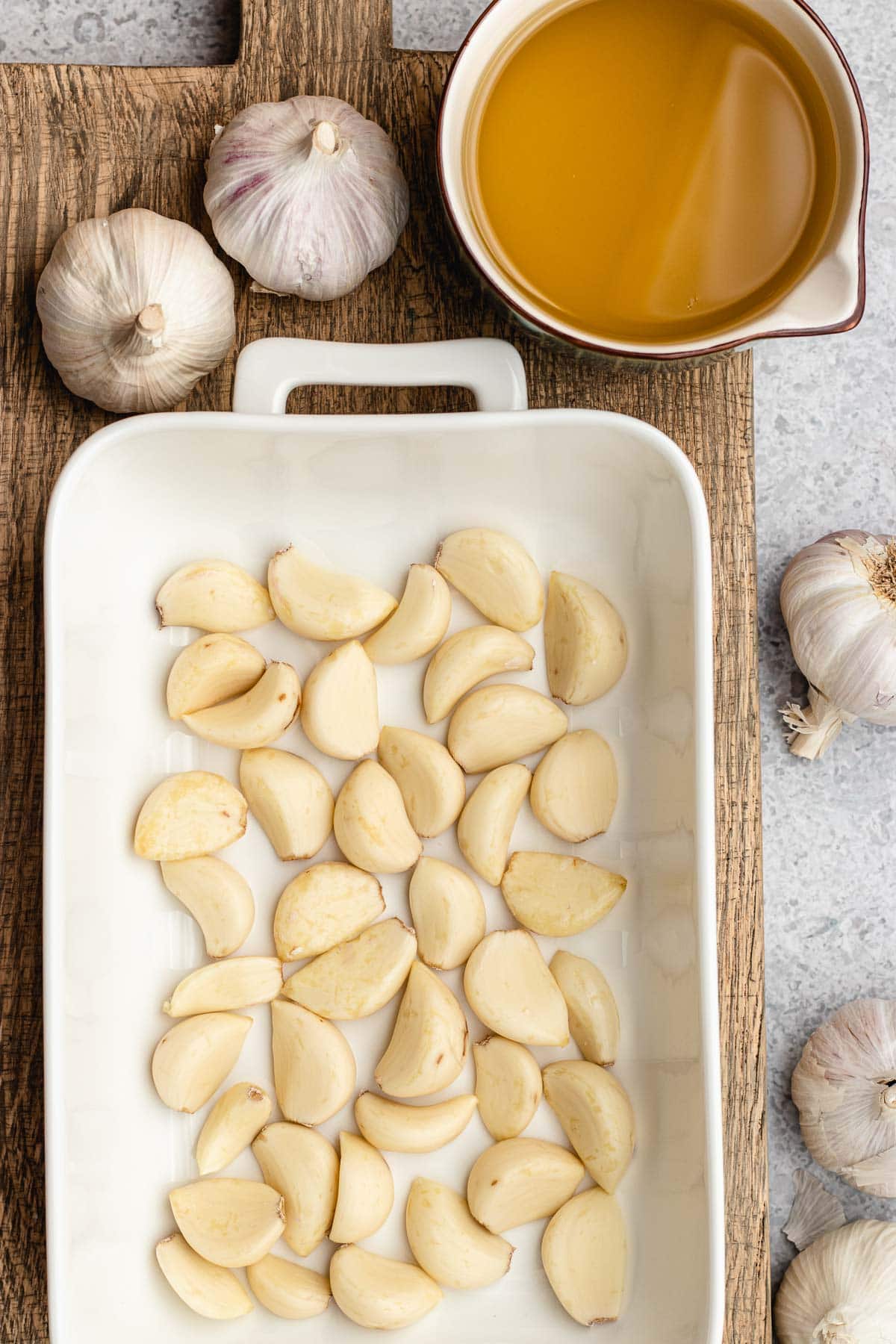 Garlic Confit raw cloves of garlic in baking dish, whole cloves and oil in measuring cup next to dish