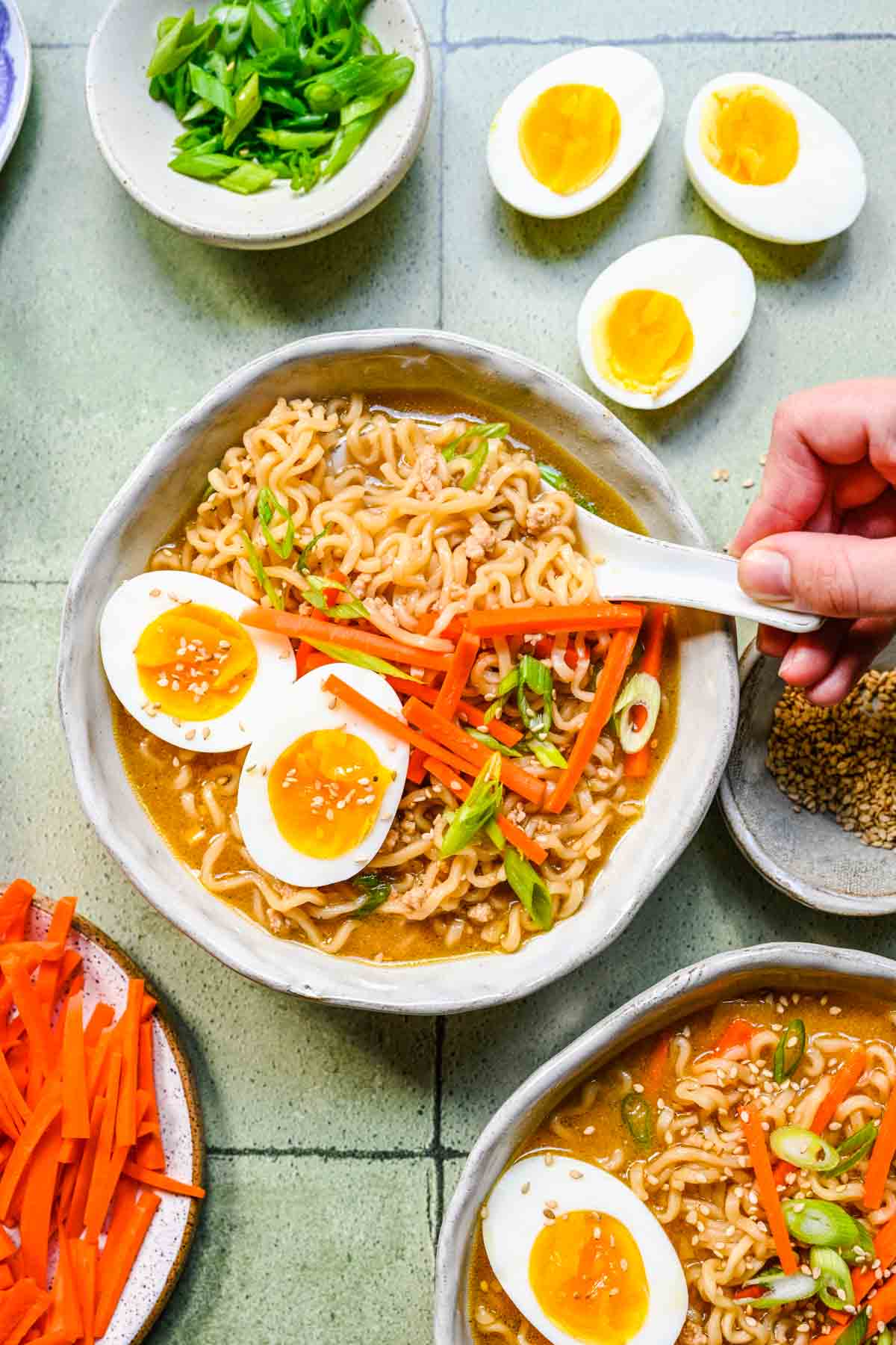 Miso Ramen finished soup in bowls with toppings, garnishes spread around decoratively, spoon scooping ramen