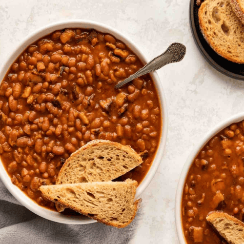 White bowl of beans with bread and a spoon