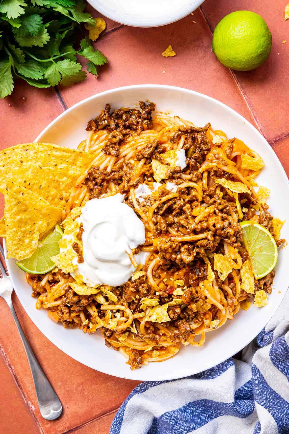 Taco Spaghetti finished pasta dish in bowl with chips, lime, and sour cream garnish