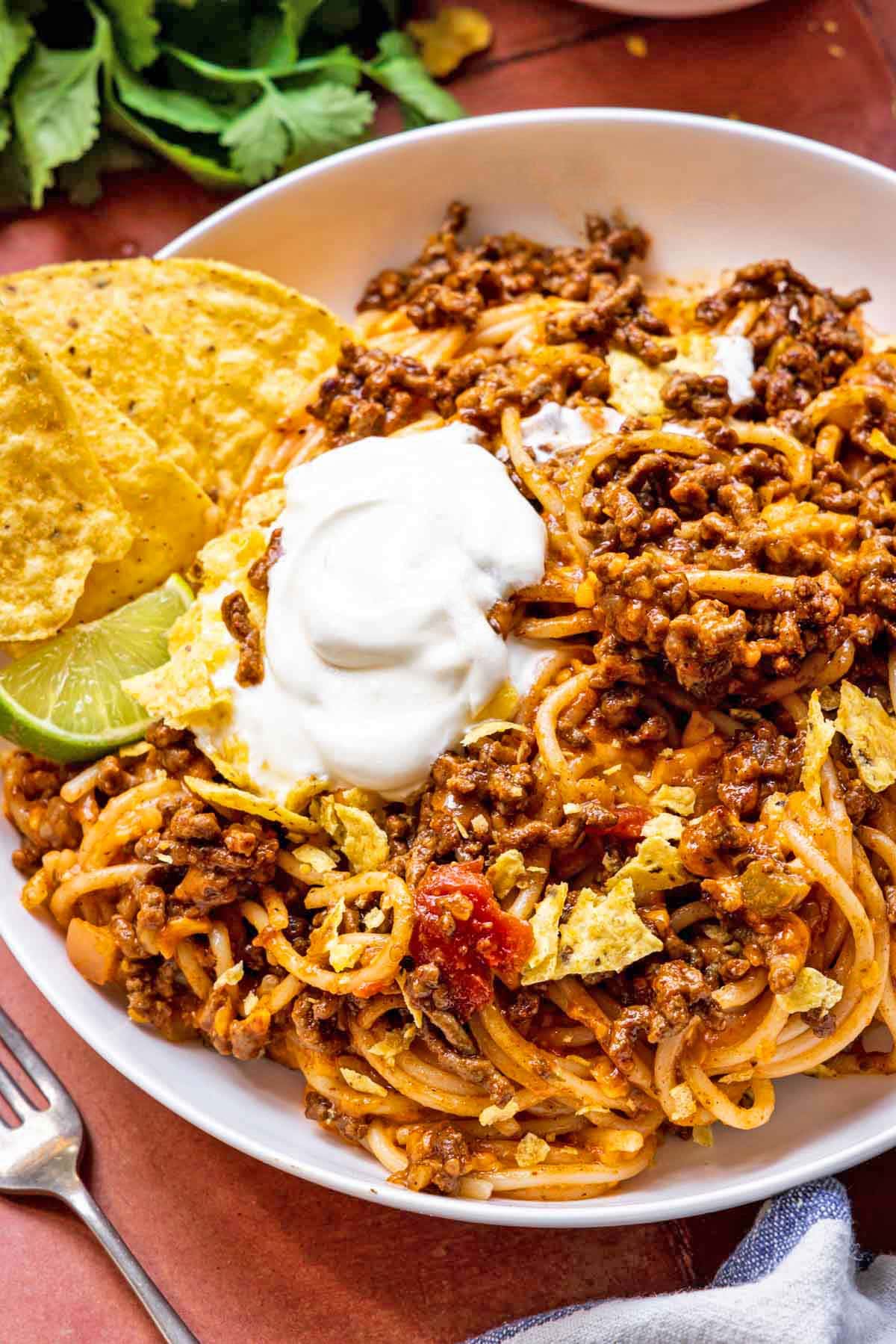 Taco Spaghetti finished pasta dish in bowl with chips, lime, and sour cream garnish