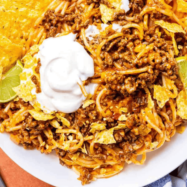 plate of pasta with sour cream on top and served with a lime wedge and chips